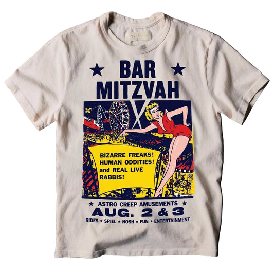 An off-white crewneck t-shirt featuring a vintage-style comic book graphic for 'Bar Mitzvah' at 'Astro Creep Amusements', laid flat on a dark textured background.