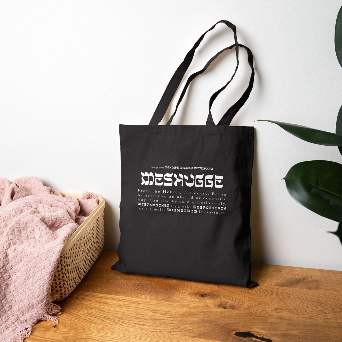 Black Meshugge definition tote lying against a wall