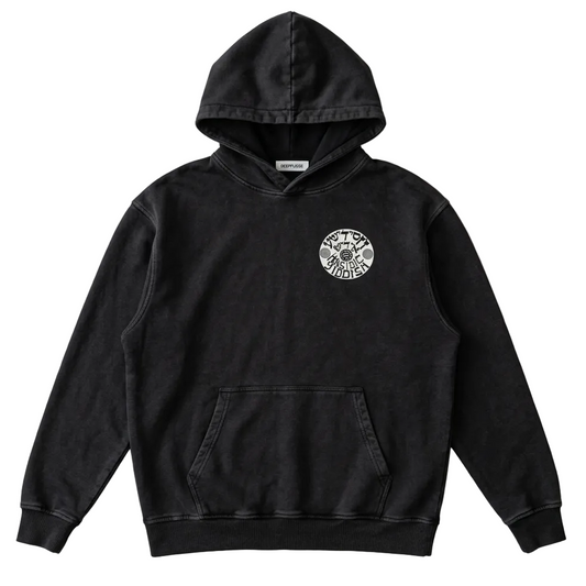 A black washed pullover hoodie with a circular white graphic on the left chest, laid flat on a light gray fabric background.