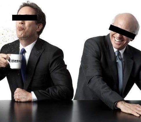 Two men seated at a table back against each other. The man on the left holds a white Meshugge mug while spitting his coffee.
