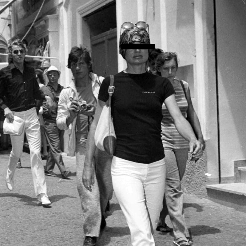 Black and white photo of a woman walking outdoors with people around her.