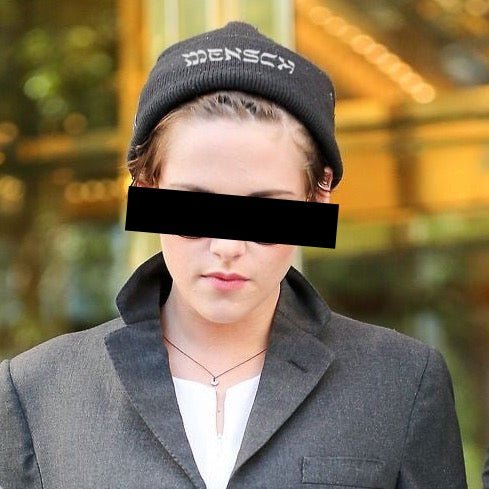 A person wearing a black knit beanie with the brand name 'MENSAH' embroidered in white on the front, a dark gray blazer, and a white top. The person's eyes are obscured by a solid black rectangular block.